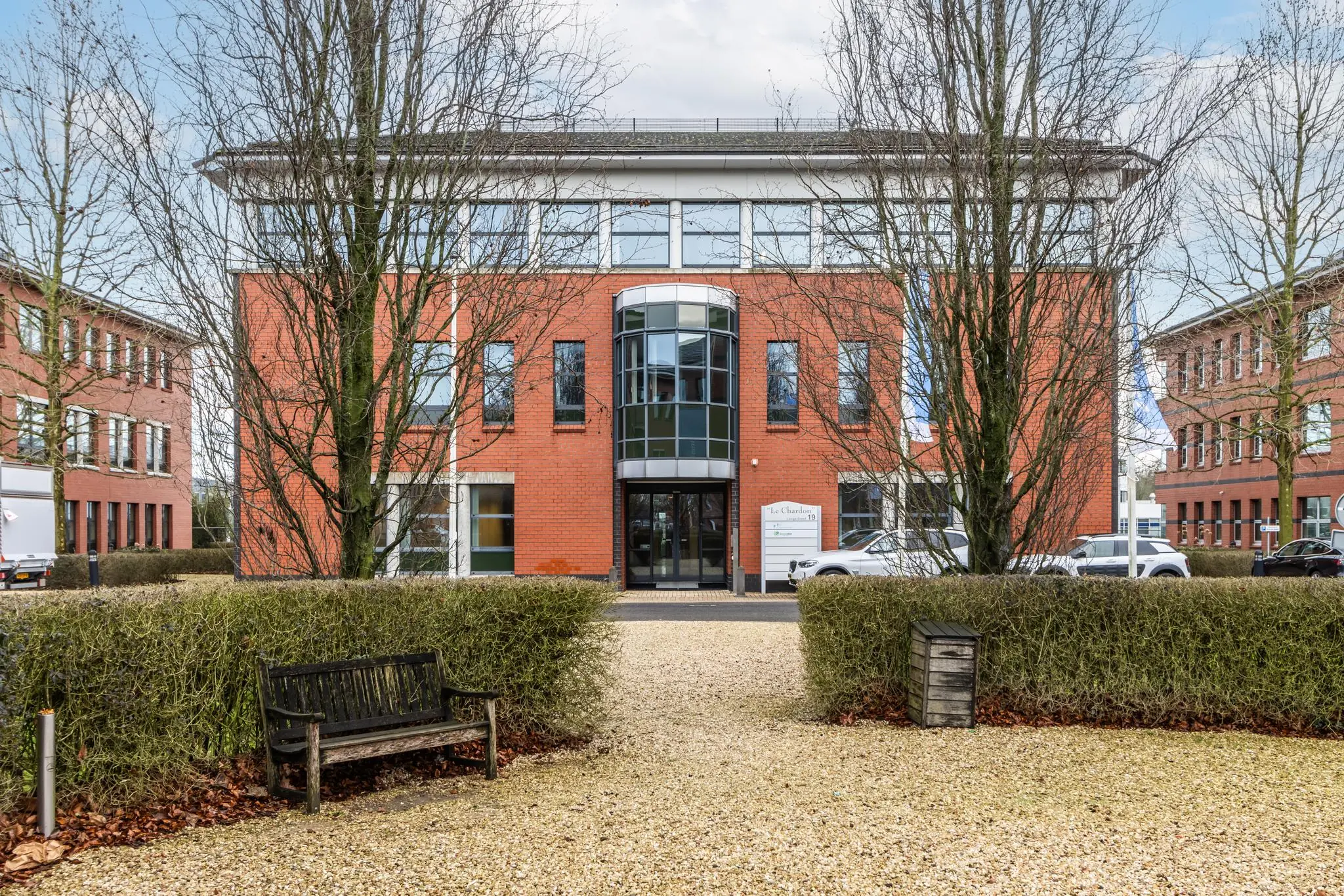 Kantoorgebouw aan de Lange Dreef met rode bakstenen gevel en glazen entree, omgeven door bomen en geparkeerde auto's.
